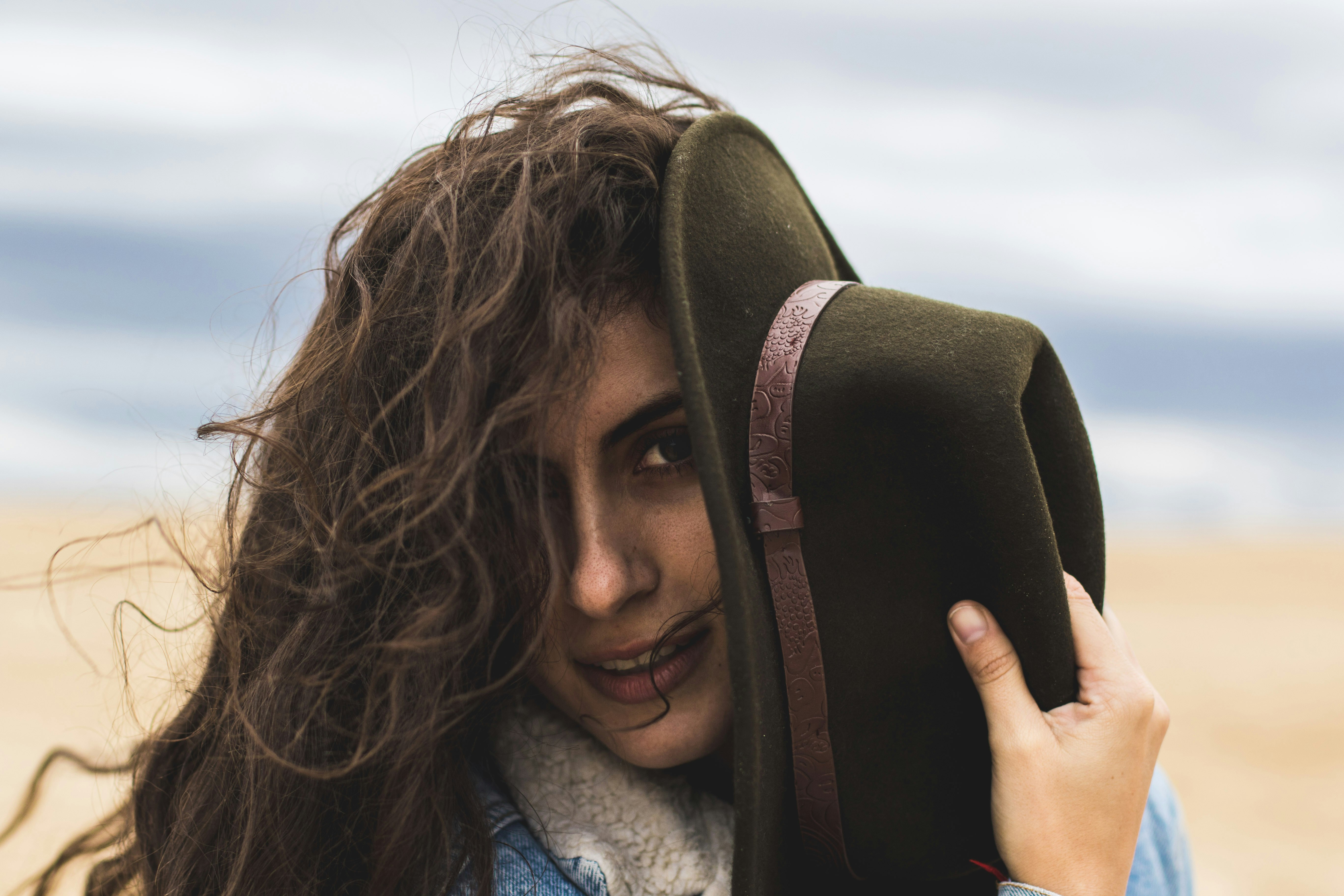 woman holding black hat on seashore during daytime